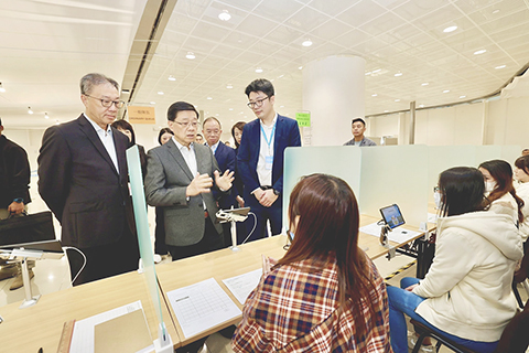 ◎ 十二月六日,香港特區行政長官李家超(前排中)視察立法會換屆選舉投票站,與工作人員交流。(香港特區行政長官辦公室供圖)