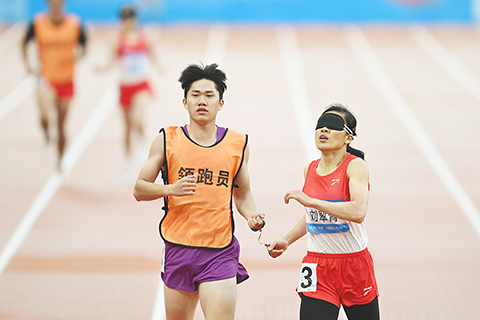 ◎ 十二月十三日,劉翠青在全國第十二屆殘疾人運動會暨第九屆特殊奧林匹克運動會田徑女子四百米T11級決賽中奪得金牌。圖為劉翠青(右一)和領跑員陳聖明衝線瞬間。(中新社記者 陳楚紅 攝)